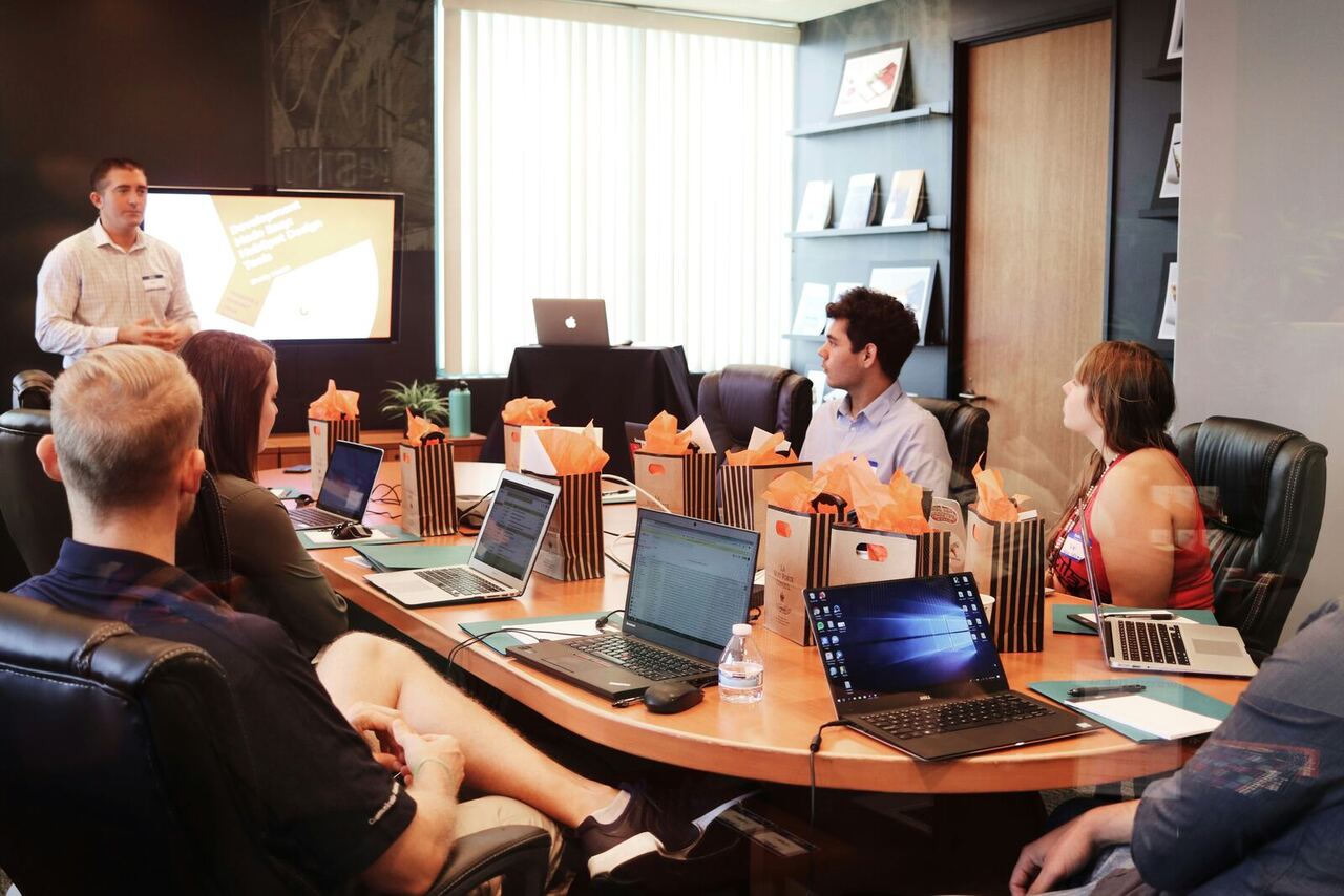 A presenter briefing a small seated group with laptops during a training session