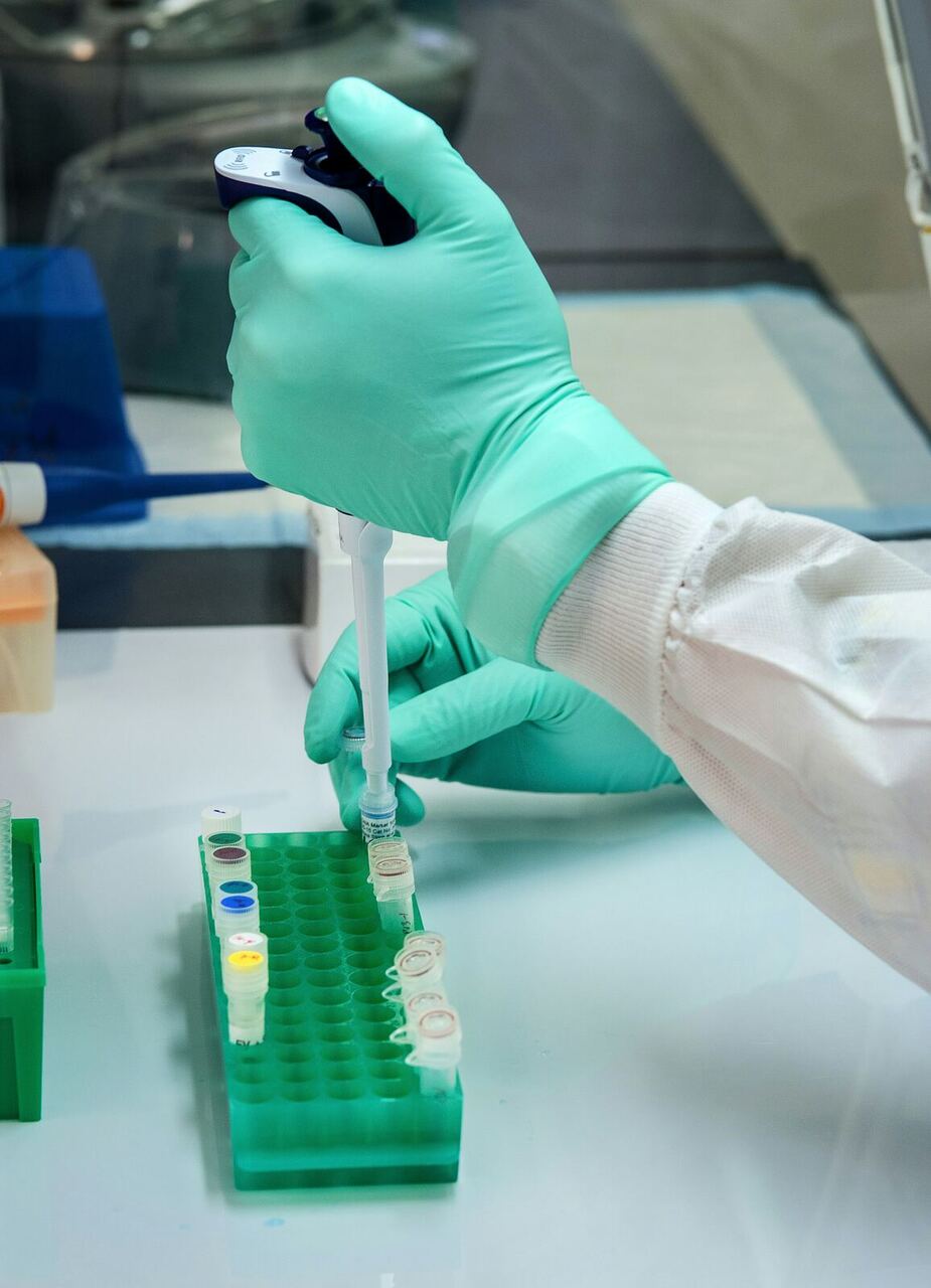 Gloved hand pipetting a sample into a lab test-tube rack, representing quality management systems work